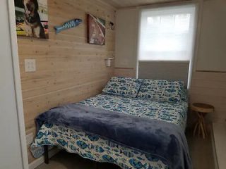 A rustic bedroom with wood-paneled walls featuring a bed with blue and sea life patterned bedding and a colorful surfboard decor on the wall