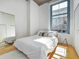 A minimalist bedroom with a large bed, white linens, and a bright window offering natural light.