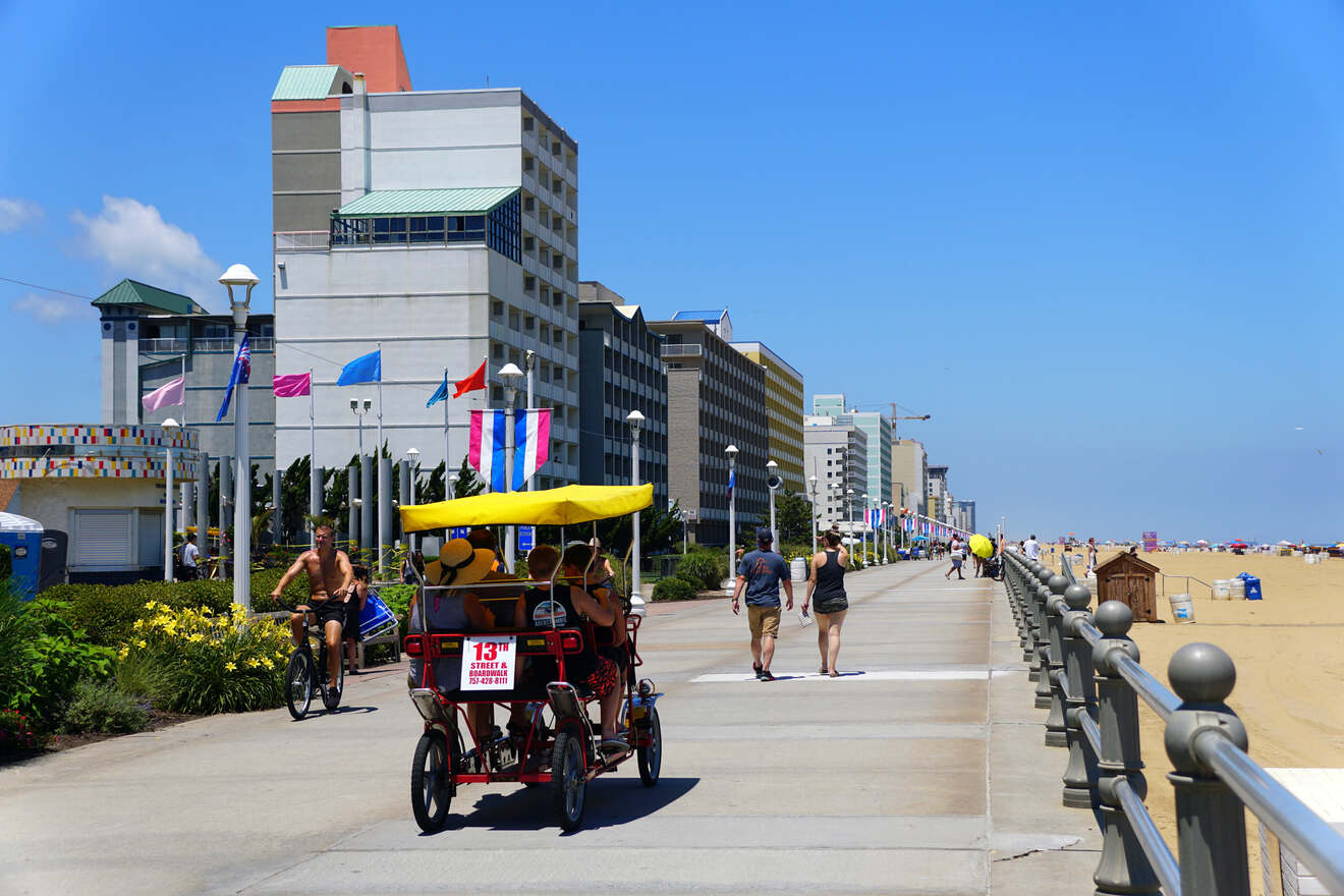 A sunny boardwalk scene with beach-goers and a pedal cab, lined by hotels and leading to the expansive Virginia Beach shoreline