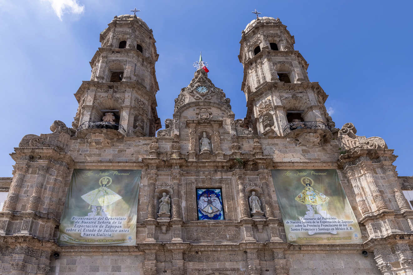 Historic stone facade of the Basilica of Our Lady of Zapopan with twin bell towers and religious banners celebrating the Bicentennial of the state of Jalisco