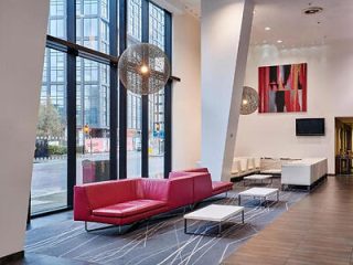 Stylish modern hotel lobby with high ceilings and large windows, furnished with a red leather couch and abstract wall art, giving a view of the urban street outside