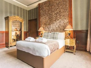 An elegant hotel room with a plush bed, golden accents, and a unique textured wall panel