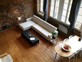Spacious loft apartment with exposed brick walls, a large white sectional sofa, and a dining area with natural light streaming in through tall windows