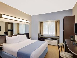 Modern hotel room with a large bed, work desk, and flat-screen TV, featuring neutral tones and clean lines
