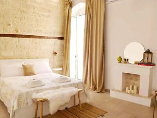 A cozy, minimalist bedroom with a white color palette and a rustic bench at the foot of the bed