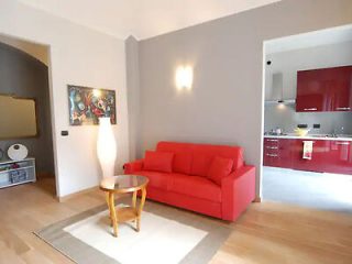 Minimalist living room with a bold red couch, wooden floors, and a small round coffee table.