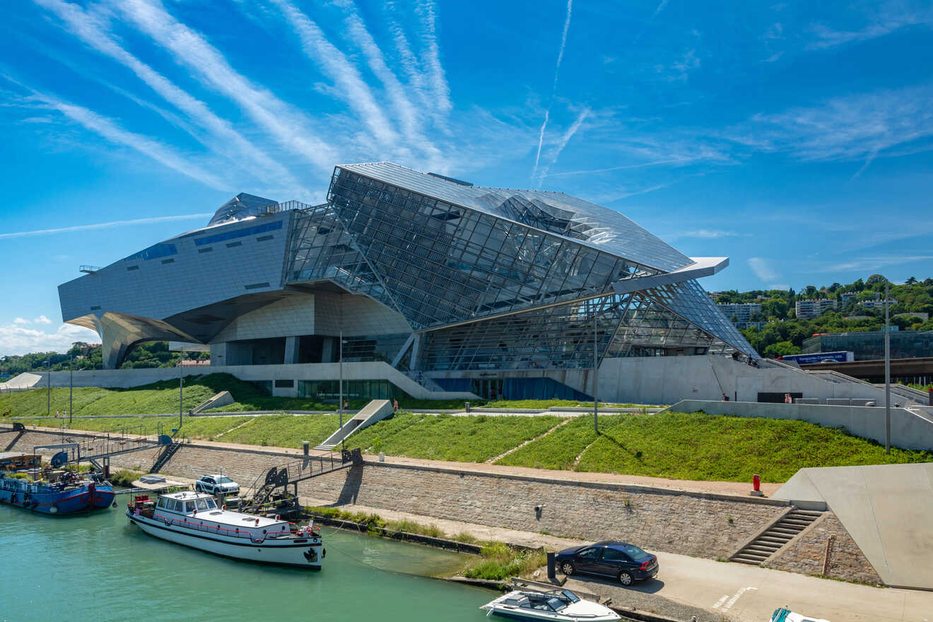 The Musée des Confluences in Lyon, France, featuring a futuristic design with metal and glass facades under a strikingly blue sky with streaky clouds