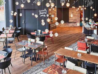 Trendy hotel restaurant interior with eclectic hanging lights, diverse seating arrangements, and a brick wall, creating a modern and inviting atmosphere