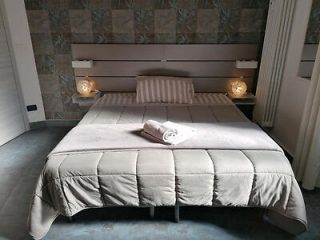 A modern bedroom in B&B Il Sogno featuring a large bed with a padded headboard and beige bedspread, flanked by warm glowing bedside lamps, set against a wall with decorative tiles.
