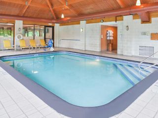 Indoor swimming pool with lounge chairs and accessible entry steps, enclosed in a wood-beamed space