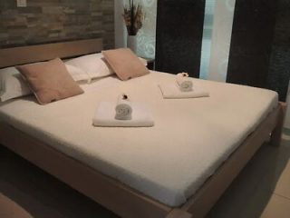 A neatly made bed with beige and white pillows, rolled towels, and decorative touches in a softly lit room.