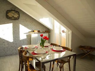 A well-lit dining room with a rustic vibe, featuring a white brick wall, a wooden table set for a meal with red tulips as the centerpiece.