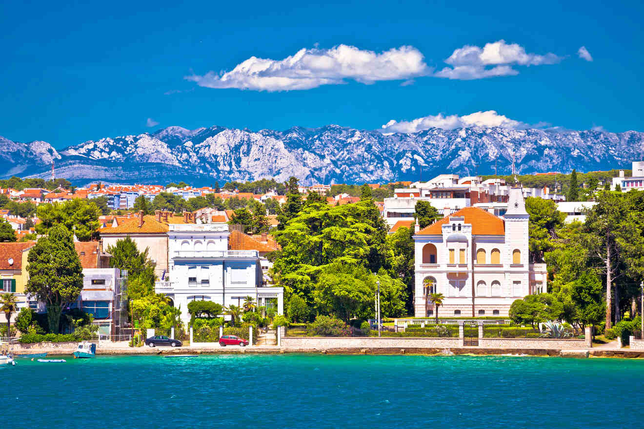 A scenic coastal area with beautiful old buildings, lush greenery, and a mountain range in the background.