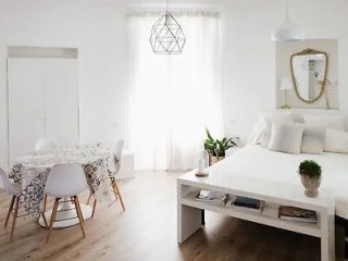 A bright and airy studio apartment with white decor, a large window, and minimalistic furniture, creating a peaceful and clean space.