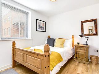 Cozy bedroom with a wooden bed frame and bright yellow accents on the bedding, accompanied by a rustic bedside table and lamp