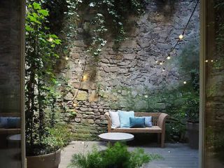 A serene courtyard garden with a rustic stone wall, wooden bench, and soft lighting, offering a tranquil urban retreat