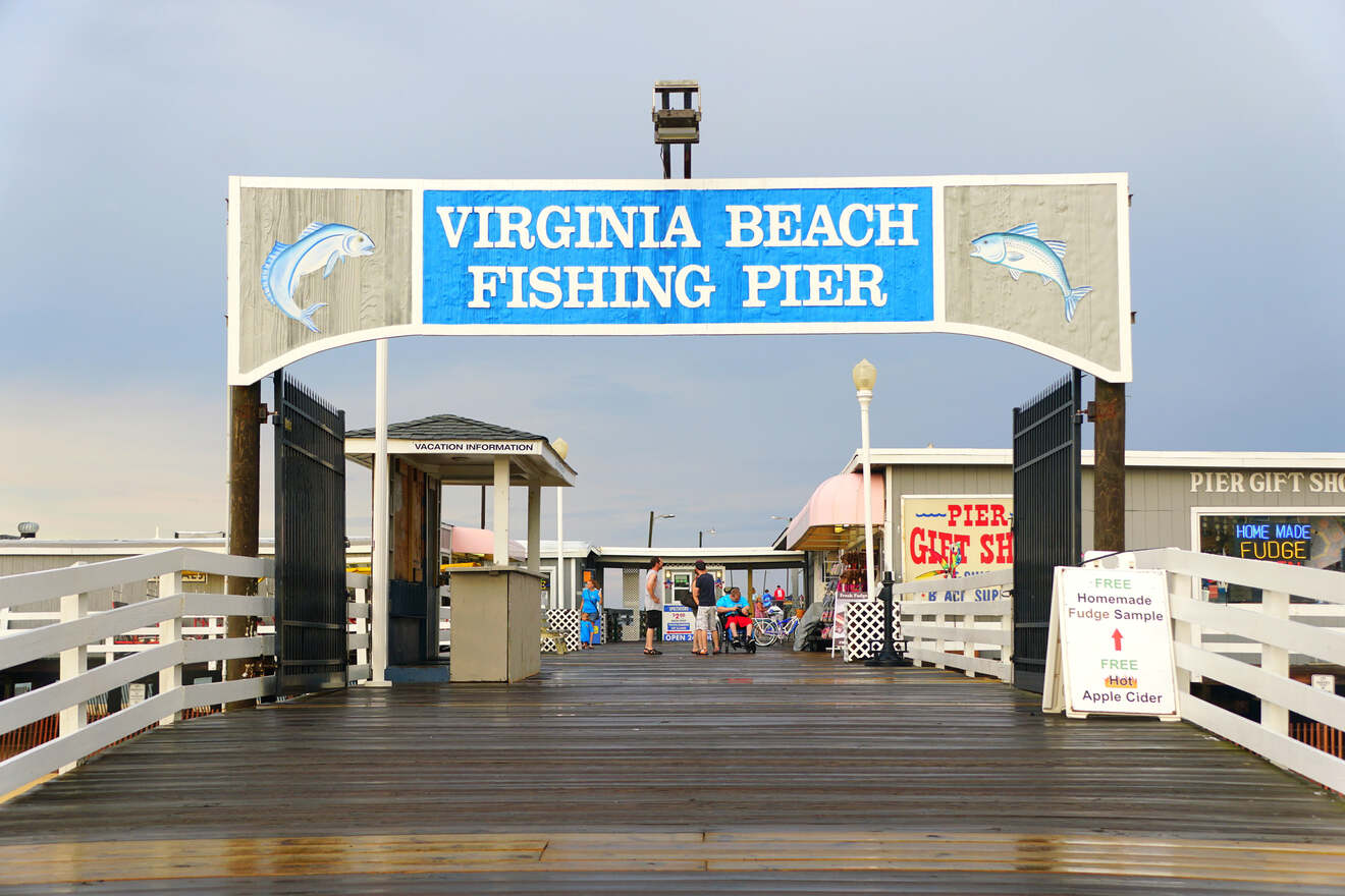 The entrance to the Virginia Beach Fishing Pier, featuring a welcome sign with fish illustrations, under a cloudy sky