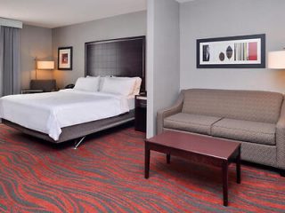 Hotel room with king-size bed and sitting area, featuring red patterned carpet and abstract wall art
