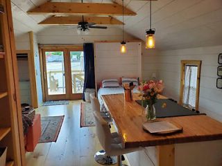 Cozy cabin interior with a wooden dining table, bed, and rustic decor, opening onto a deck