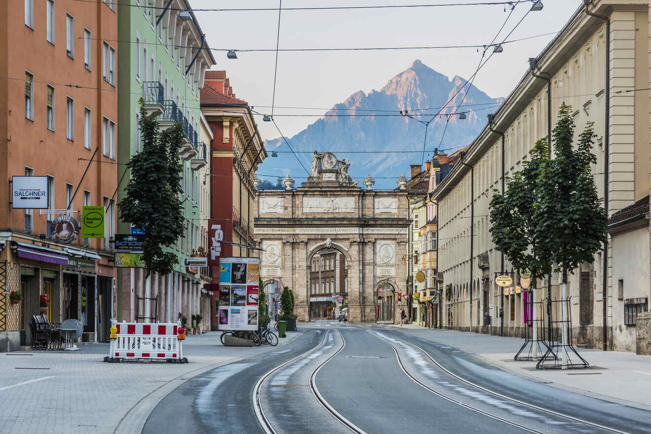 Quiet Innsbruck street with historic architecture, tram lines, and the Tyrolean mountains towering over the city