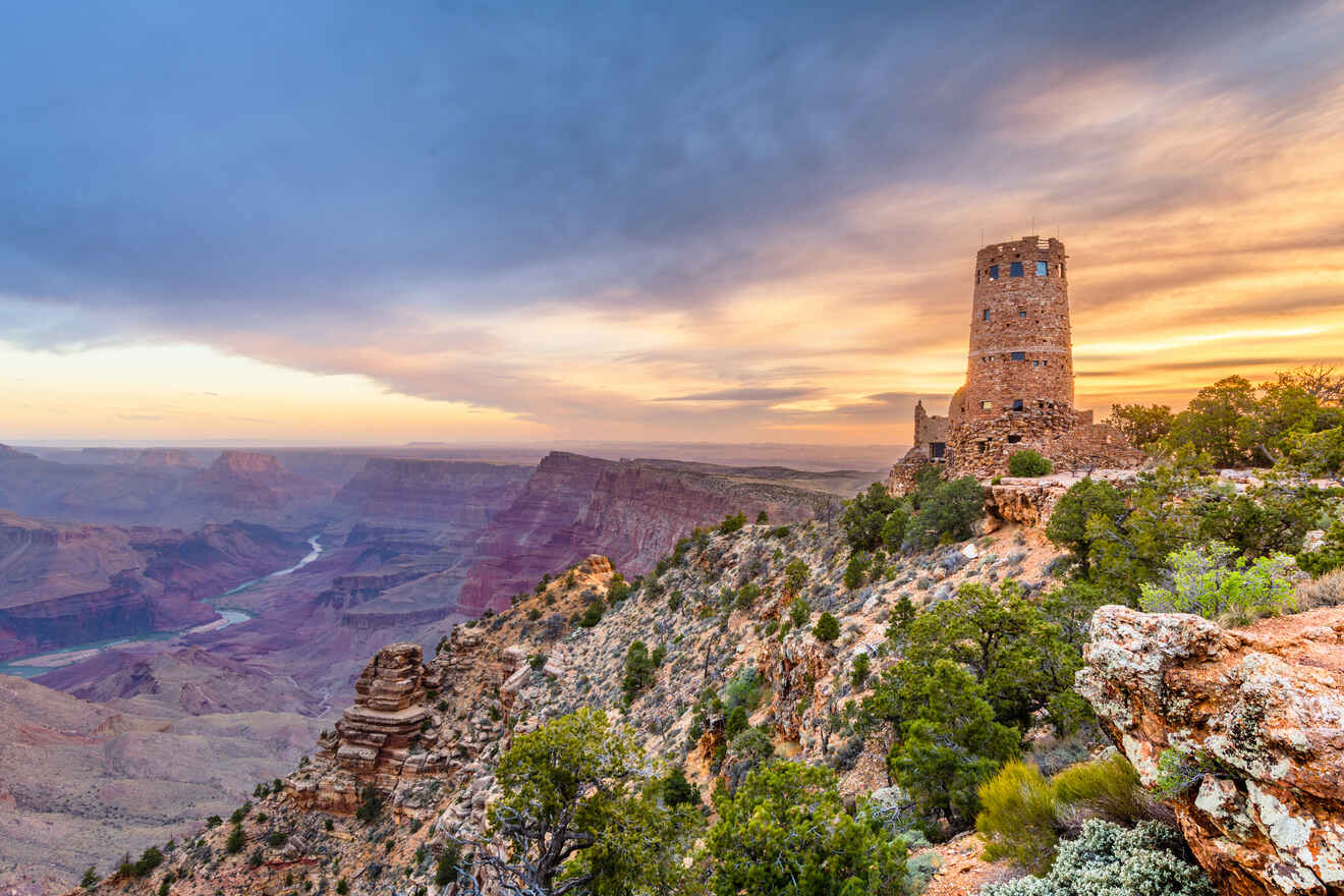 Desert View Watchtower at dusk, with its stone architecture standing tall against the expansive Grand Canyon and colorful sky.