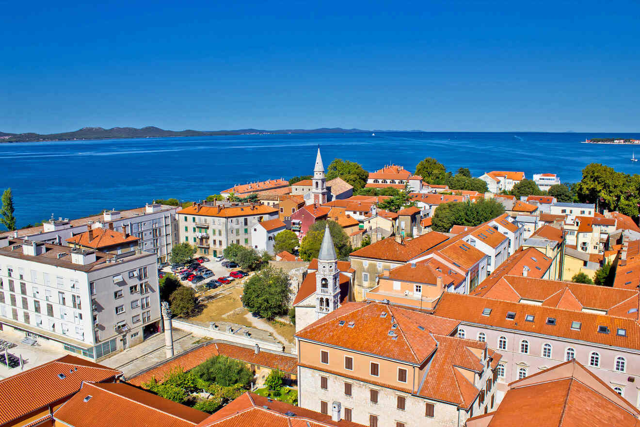 An aerial view of a coastal town with red-roofed buildings, churches, and the sea in the background.