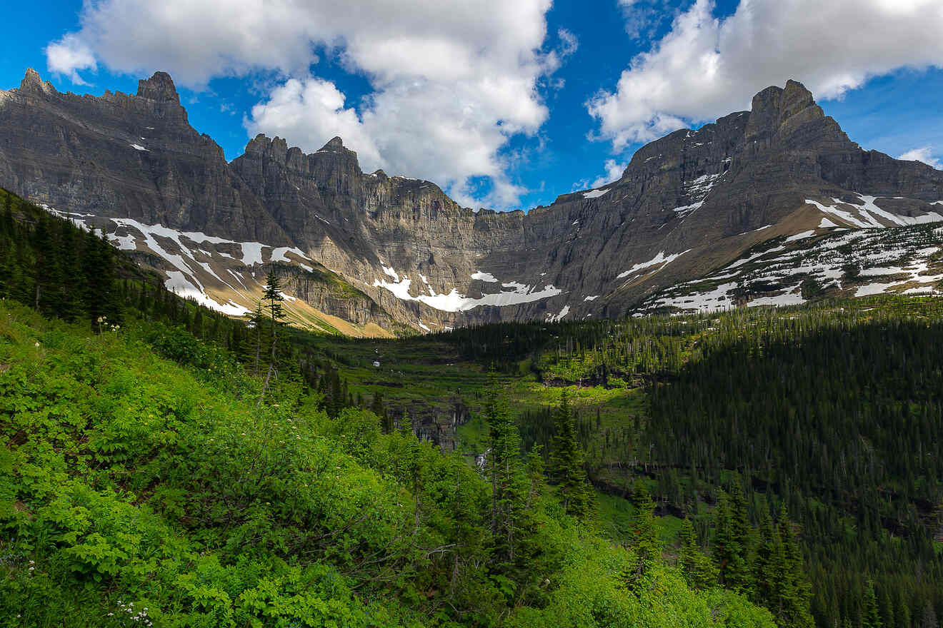 A panoramic view of Glacier National Park showcasing towering cliffs, green valleys, and a dynamic sky with light breaking through the clouds