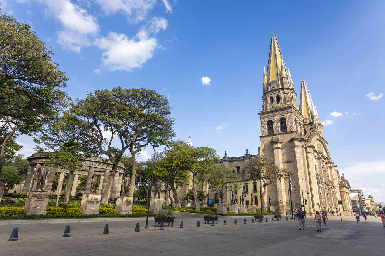 The Guadalajara Cathedral viewed from the plaza, showcasing its neo-Gothic towers, framed by lush trees and a clear sky