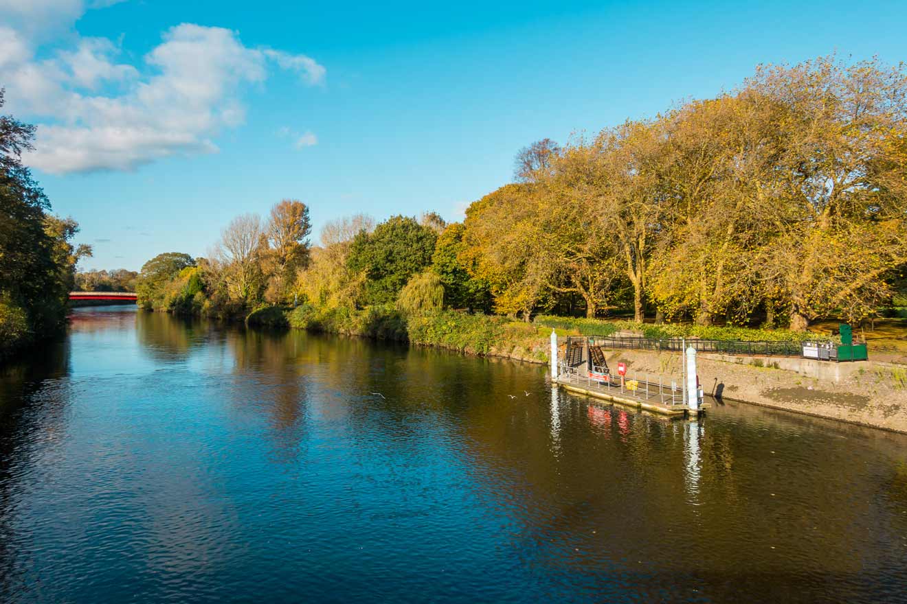 A serene riverside view with lush greenery, clear skies, and a small docking area on a sunny day