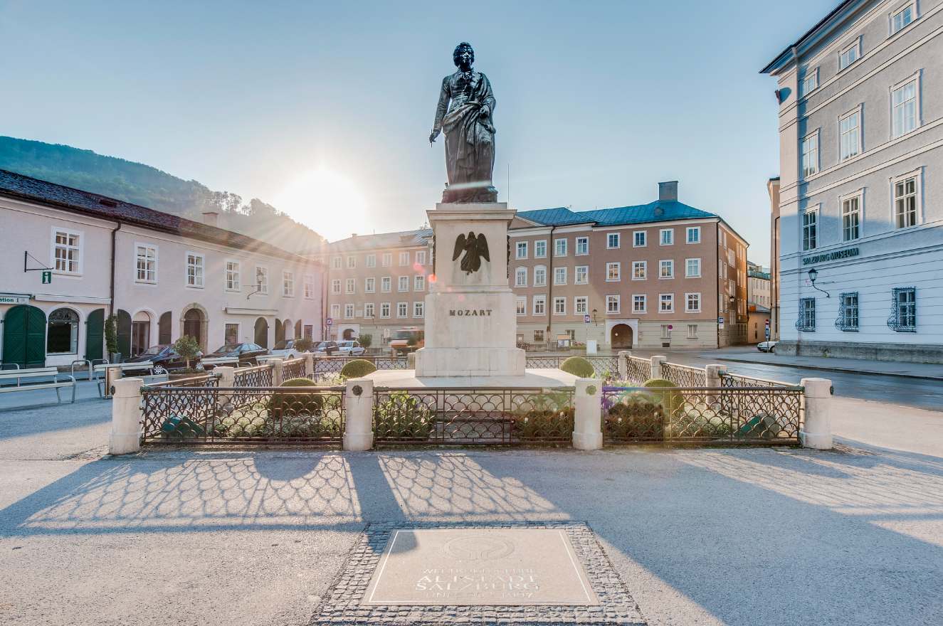 Mozart statue in Salzburg's Mozartplatz with sunburst and university building in the background