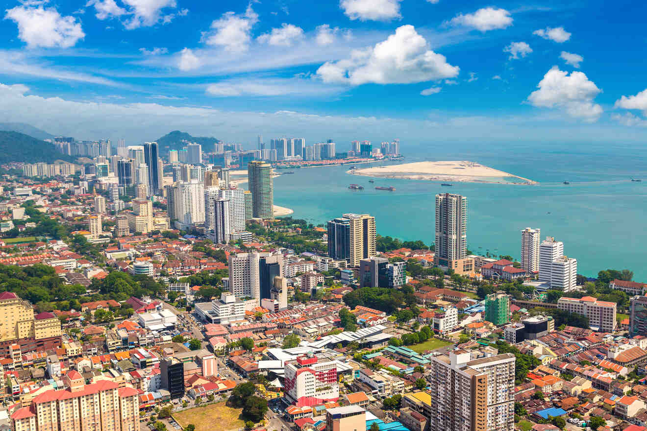 Aerial view of a coastal cityscape featuring high-rise buildings, residential areas, and calm ocean waters under a partly cloudy sky.