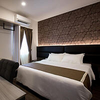 A modern hotel room with a double bed, textured accent wall, air conditioner, and a window with brown curtains.