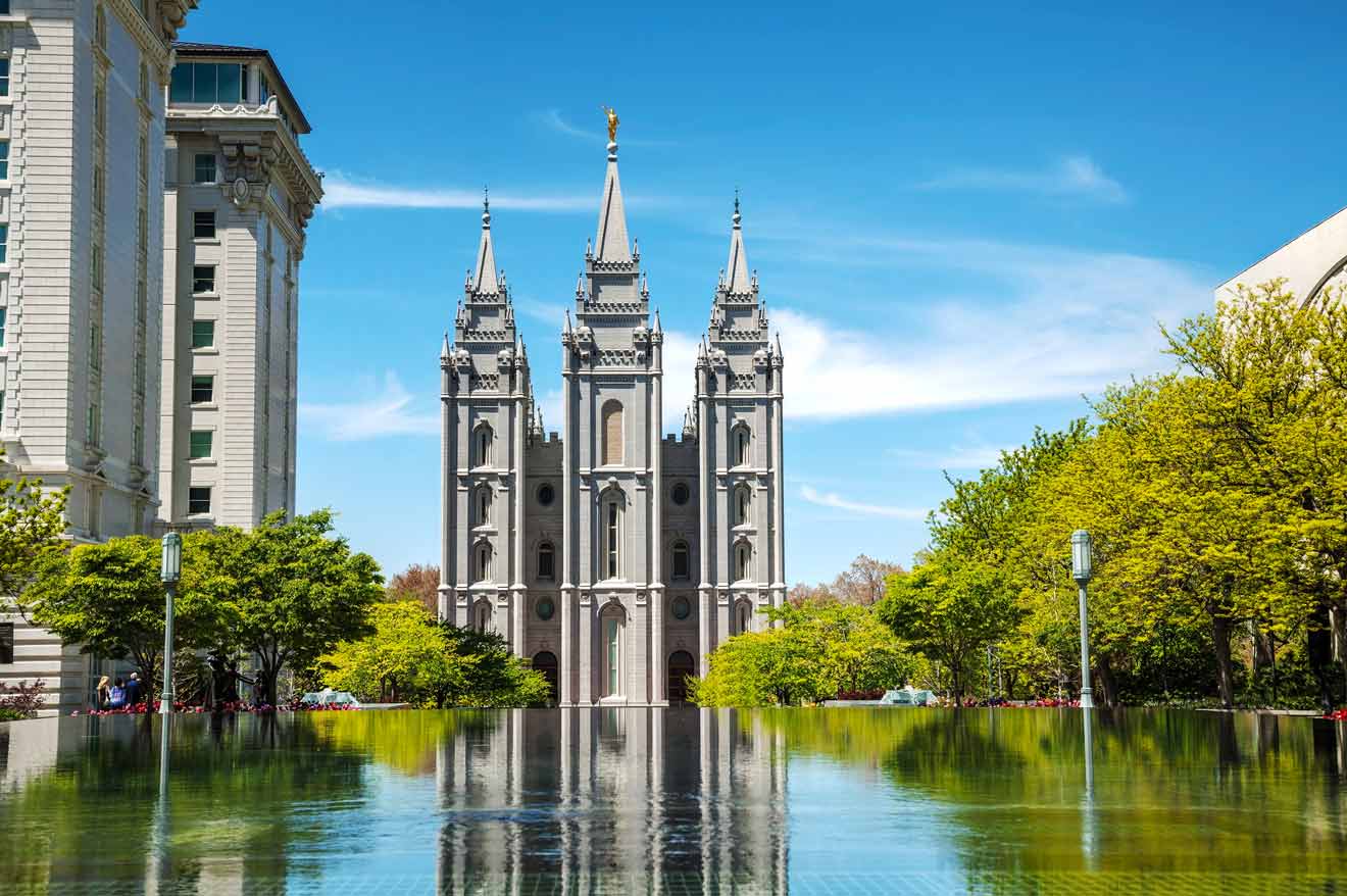 Reflection of a historic church with three spires in a pool, surrounded by trees and adjacent buildings, under a clear blue sky.