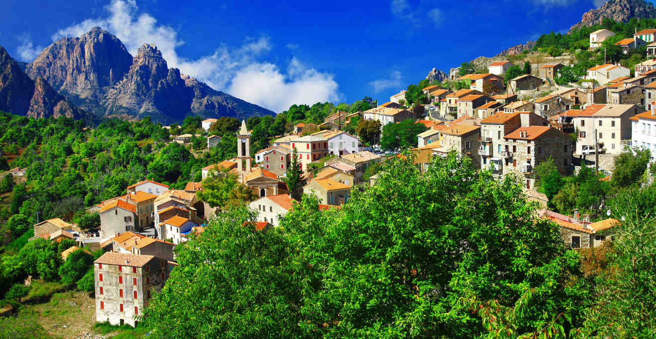 Charming village nestled in the hills with colorful houses and lush greenery, with jagged mountains rising in the background.