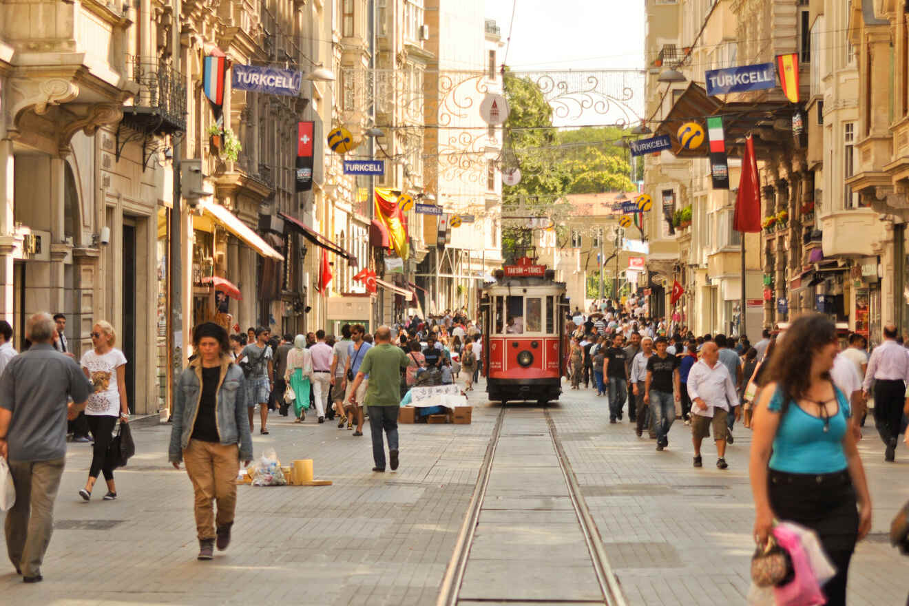 A bustling street scene in Istanbul with pedestrians, shops, and the historic red tram under a clear sky, embodying the city's lively atmosphere