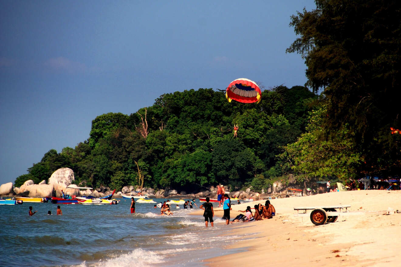People enjoying various activities on a beach with parasailing, swimming, and lounging under a clear sky.