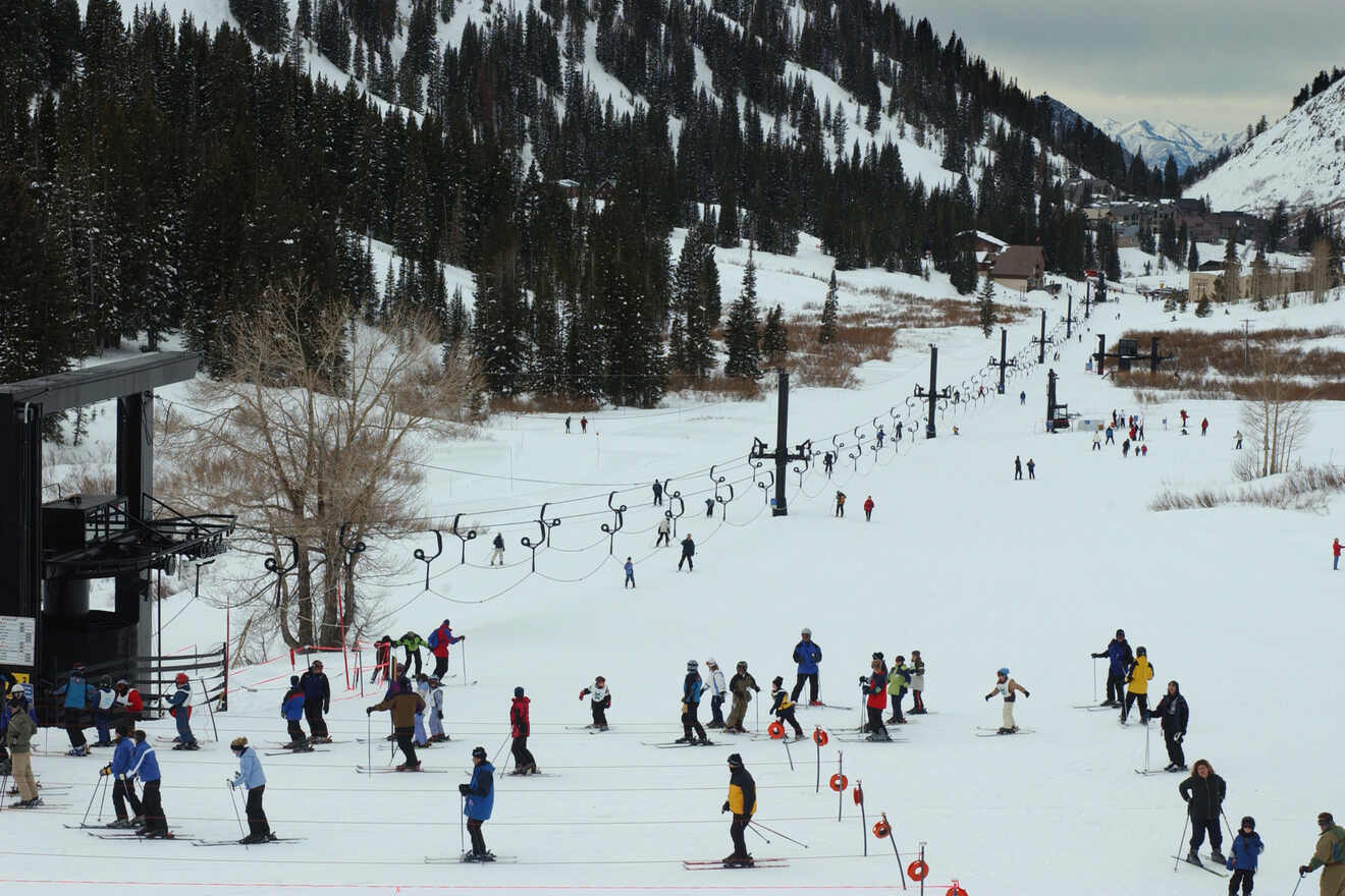 Skiers navigate a snowy slope in a mountainous area with pine trees and a ski lift.