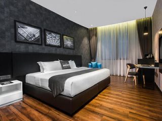 Modern hotel room with a large bed, white linens, gray headboard, and black accent wall adorned with three framed photos. Room includes a desk, chair, nightstand, and floor-length curtains.