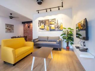A modern living room with a yellow sofa, a grey sofa, a wooden coffee table, a wall-mounted TV, a potted plant, and framed artwork on the wall.