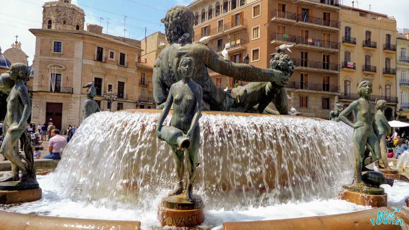 The Fountain of the Naiads in Piazza della Repubblica, Rome, featuring bronze sculptures of nymphs and a muscular male figure, set against the backdrop of classic Roman architecture and busy urban life