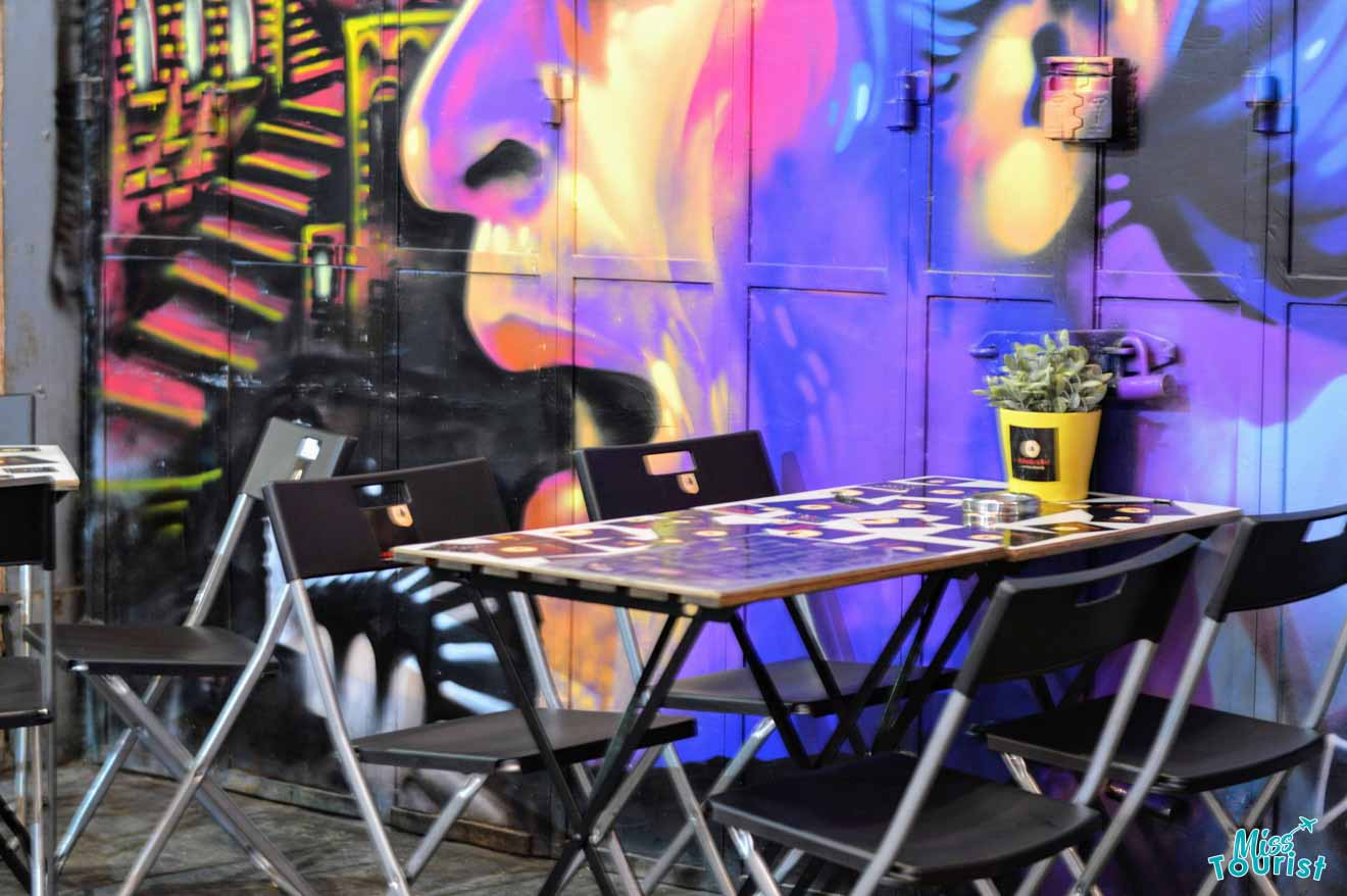 The author of this post visiting an outdoor café seating with colorful street art in the background, creating a vibrant urban atmosphere.
