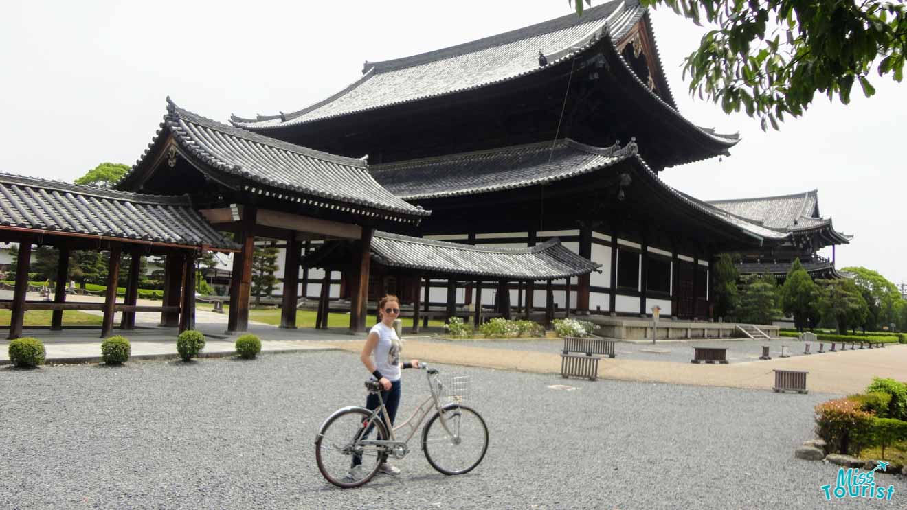 The writer of the post cycling in front of a traditional Japanese temple's spacious courtyard, shaded by lush green trees