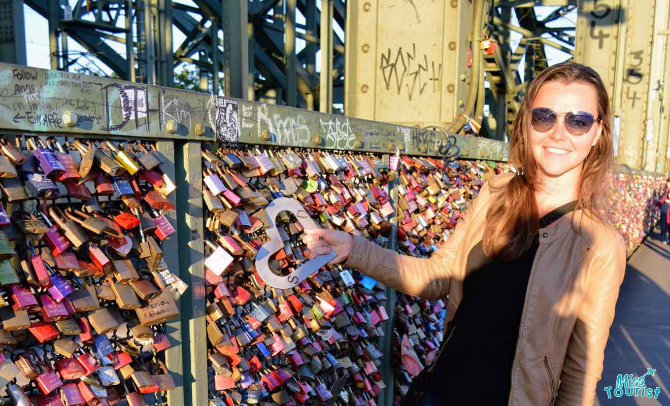 The writer of the post placing a love lock on the Hohenzollern Bridge in Cologne, with the bridge's structure and locks in the background.