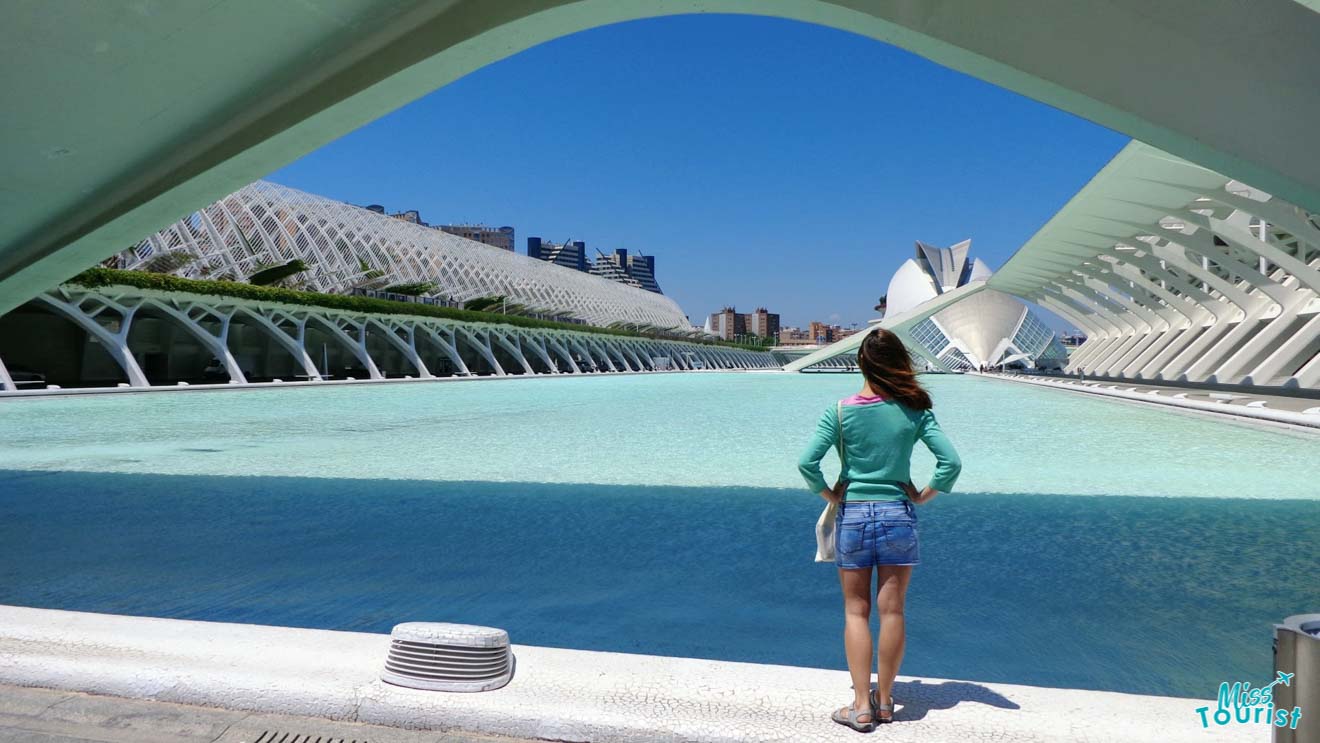 The writer in the post observing the futuristic architecture of the City of Arts and Sciences in Valencia, Spain, standing under an archway with a clear view of the surrounding structures and waterways.