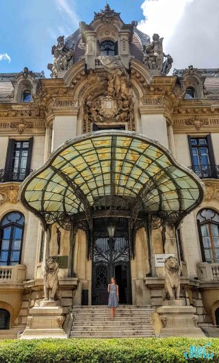 Our founder, Yulia, standing in front of a grand historical building entrance in Bucharest with ornate sculptures, a stained-glass canopy, and the writer of the article standing on the steps, emphasizing the architectural elegance.