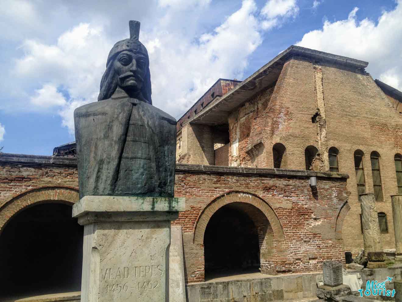 A bronze bust of Vlad Tepes (Vlad the Impaler) with the years 1456-1462 engraved, set against the backdrop of an old brick building, evoking a sense of history and legend