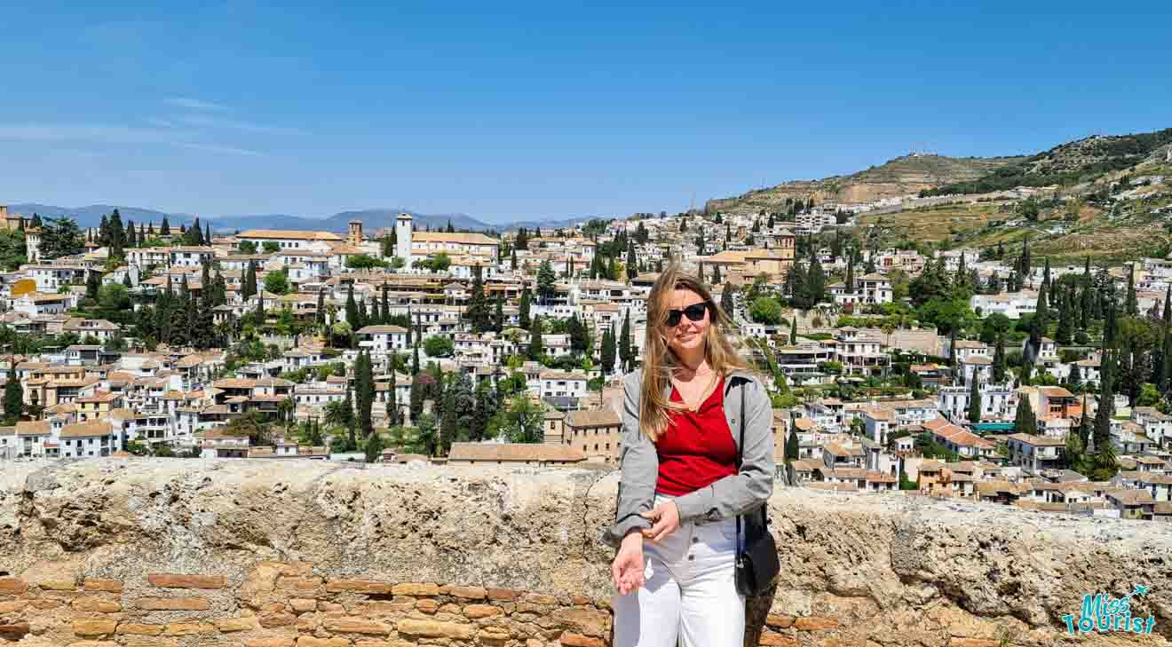 Author of the post smiling for the camera with the picturesque hillside neighborhood of Granada, Spain, as a stunning backdrop under a clear blue sky