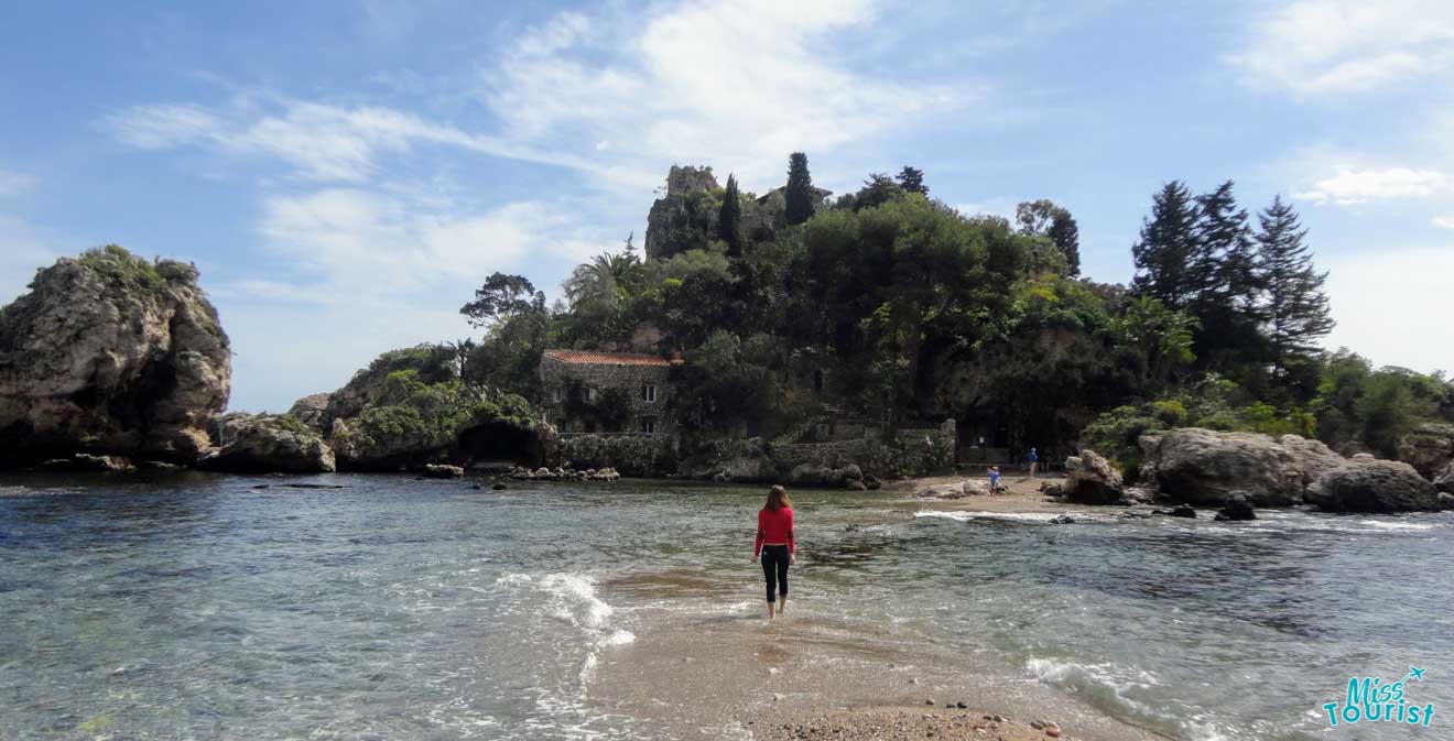 A person standing in the water near a small island.