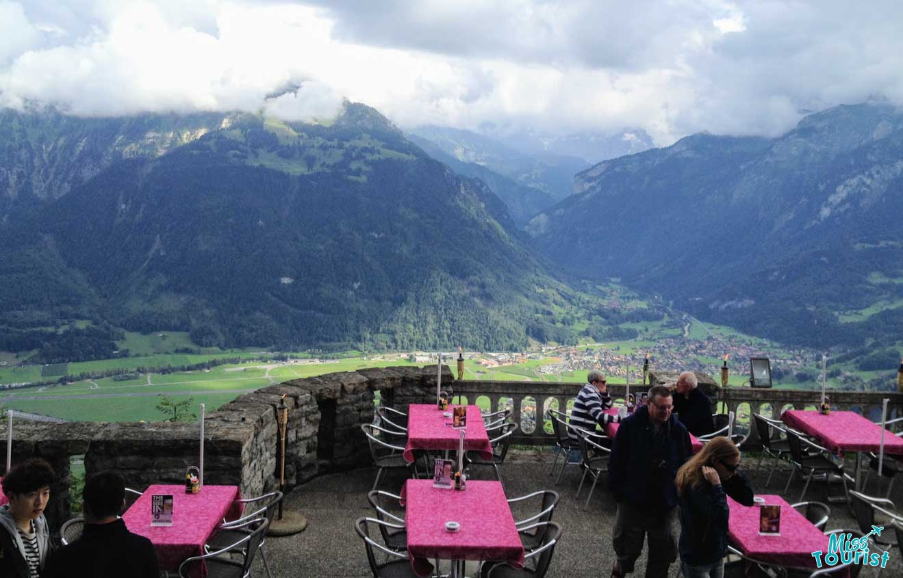 Mountain-view terrace with pink tablecloths in Interlaken, where visitors enjoy the panoramic vistas of the green valley and misty mountains