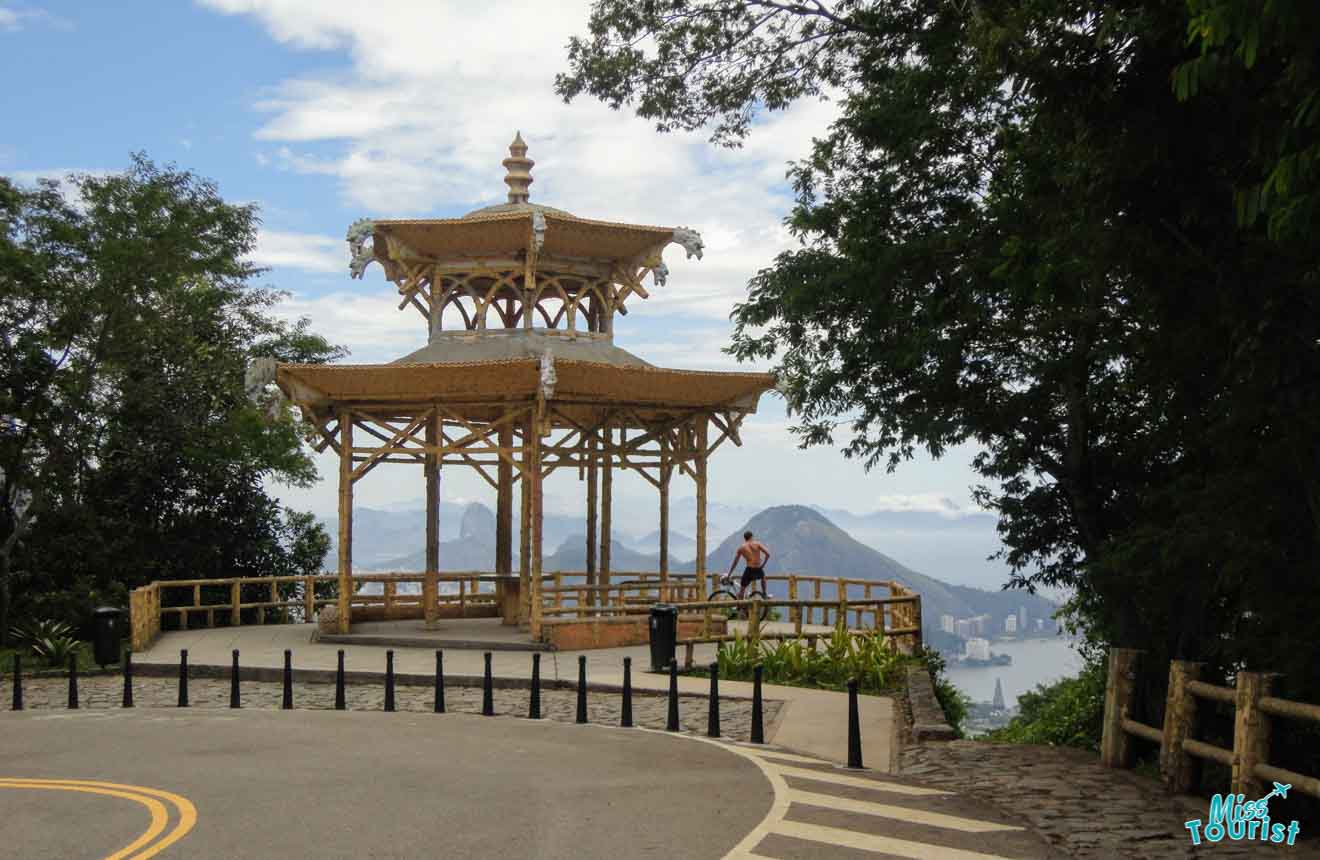 A gazebo with intricate wooden architecture at a lookout point, offering a panoramic view of Rio de Janeiro's landscape and coastline